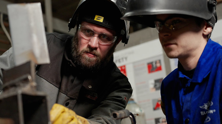 Teacher working with student, showing him how to weld.